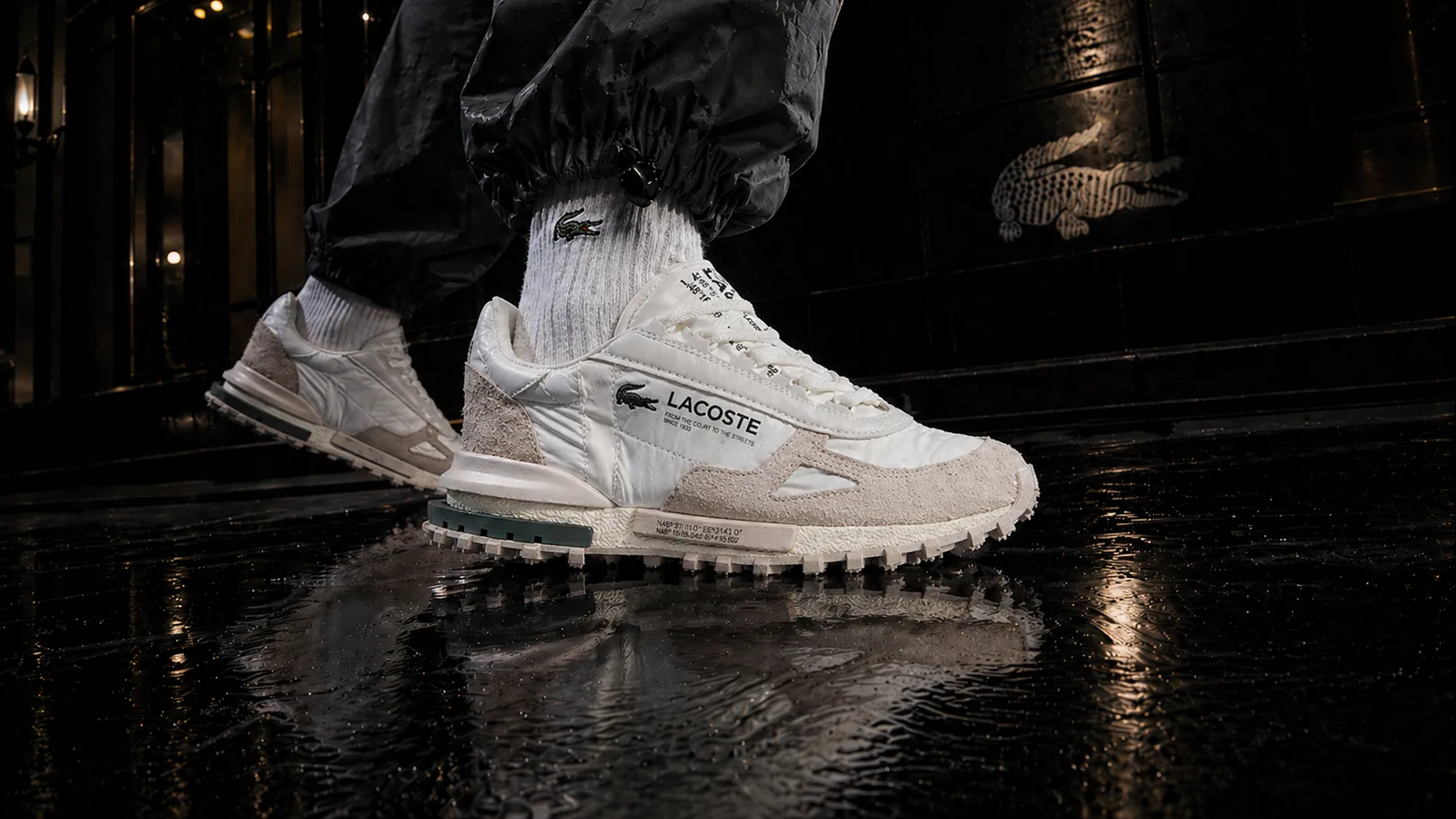 Повний образ із білими кросівками Lacoste у темній кінематографічній сцені